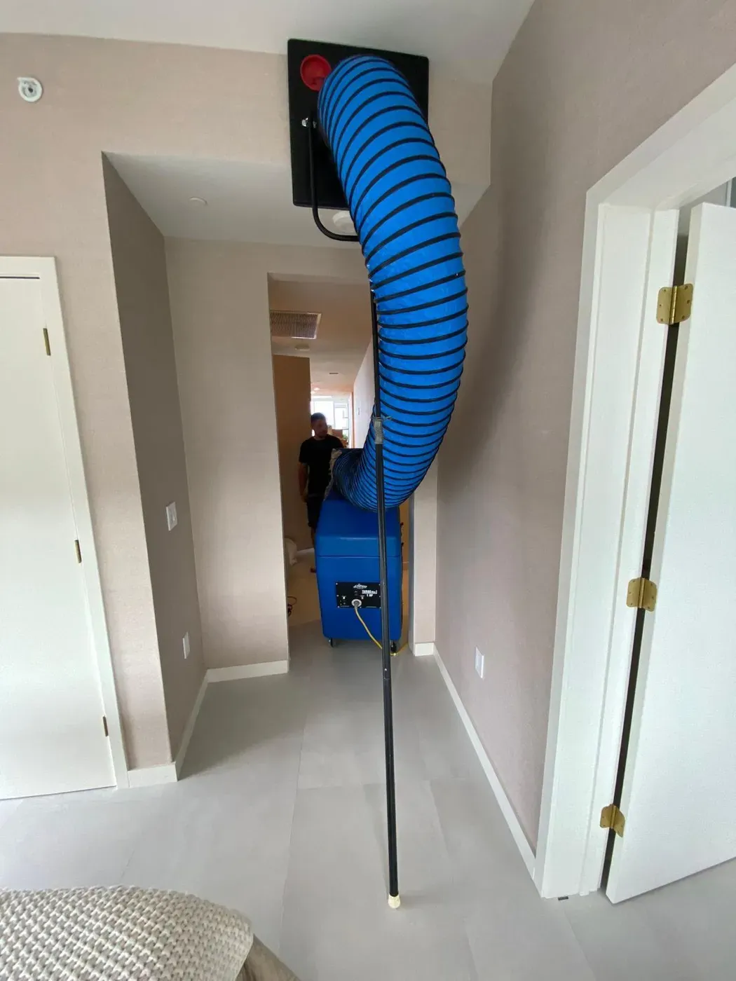 A negative-air machine connected to a ceiling vent with lay-flat duct during a duct cleaning