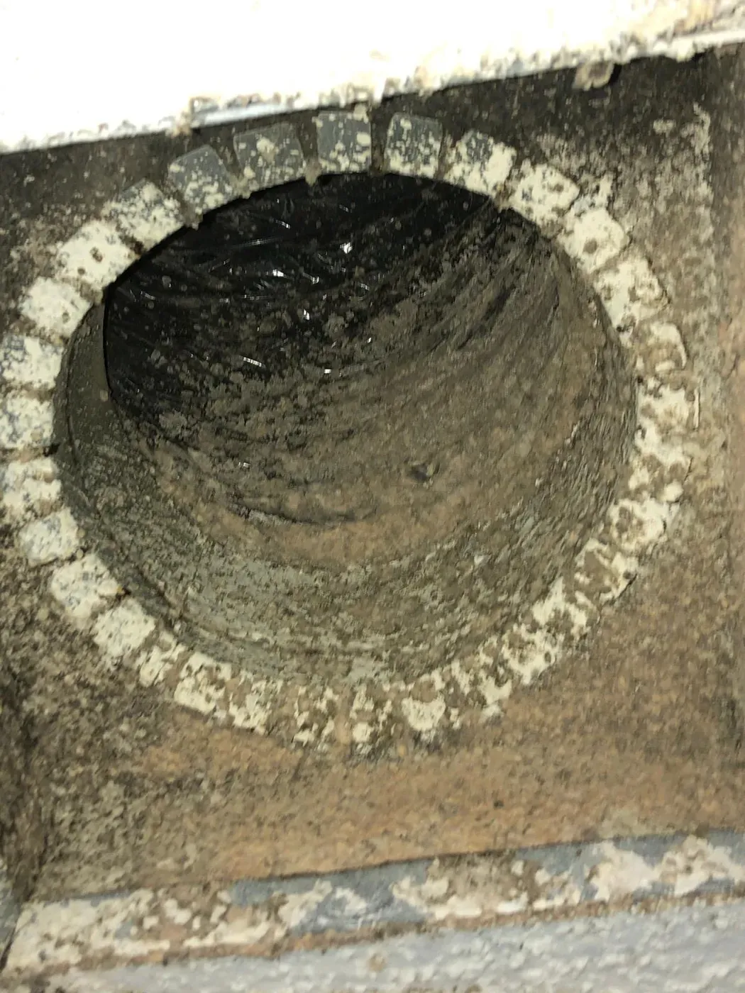 A round return-air duct boot packed with thick black dust and debris