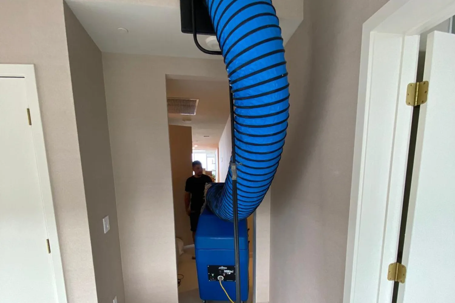 A negative-air machine connected to a ceiling supply vent with lay-flat duct, pulling dust out of a home's air duct system during a cleaning