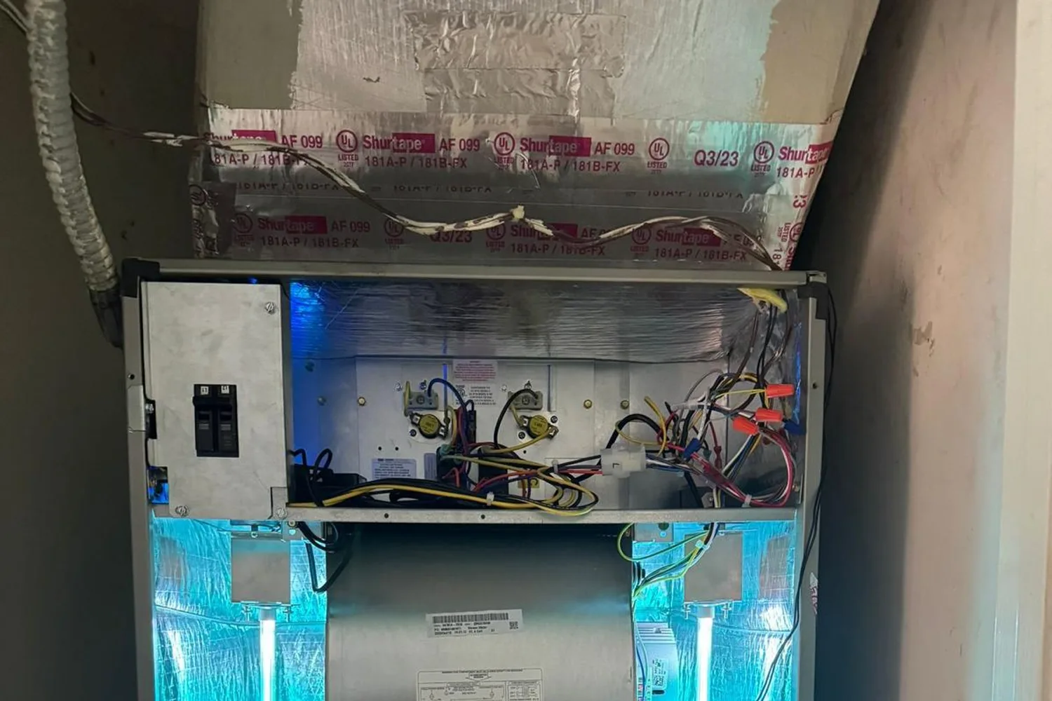 UV-C germicidal lamps glowing blue inside an HVAC air handler, installed beside the blower to sanitize the air stream